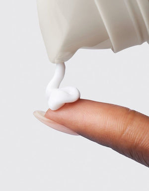 White Cleanser being pumped from bottle onto finger with grey background