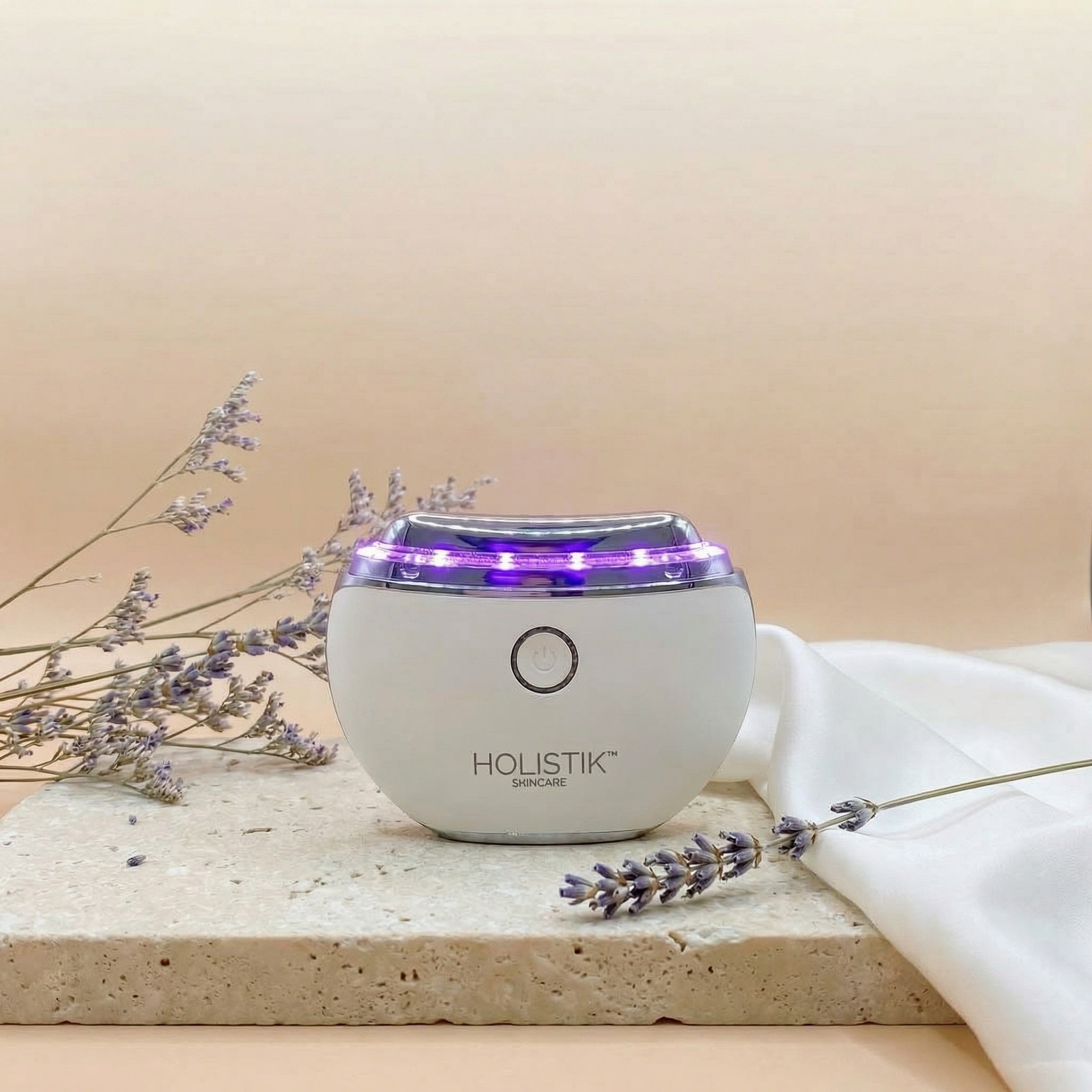 Holistik Skincare LED Gua Sha Face & Body Massage device with lavender flowers on a beige background