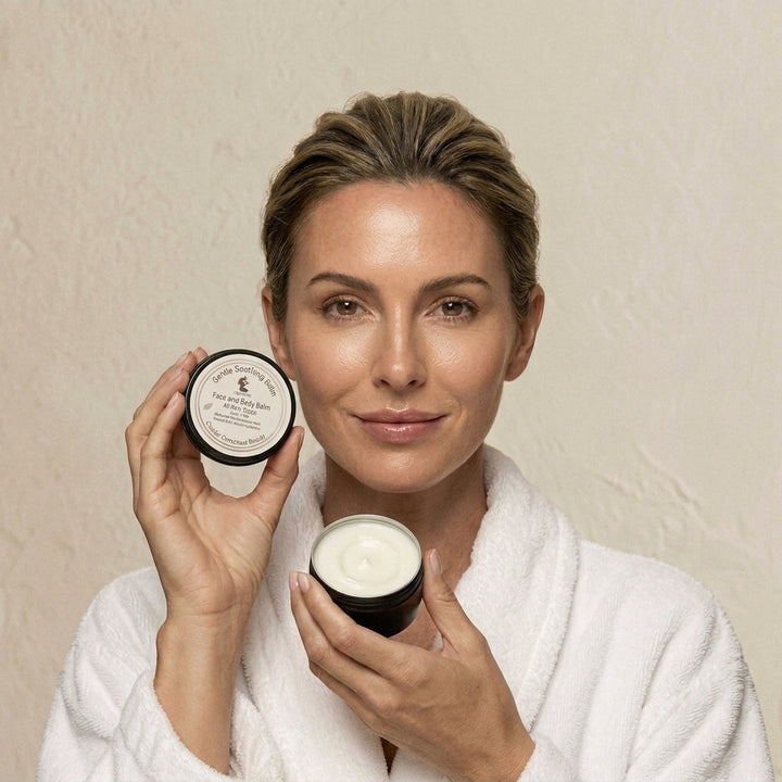 Woman in a white robe holding Holistik Skincare Gentle Soothing Balm against a beige background