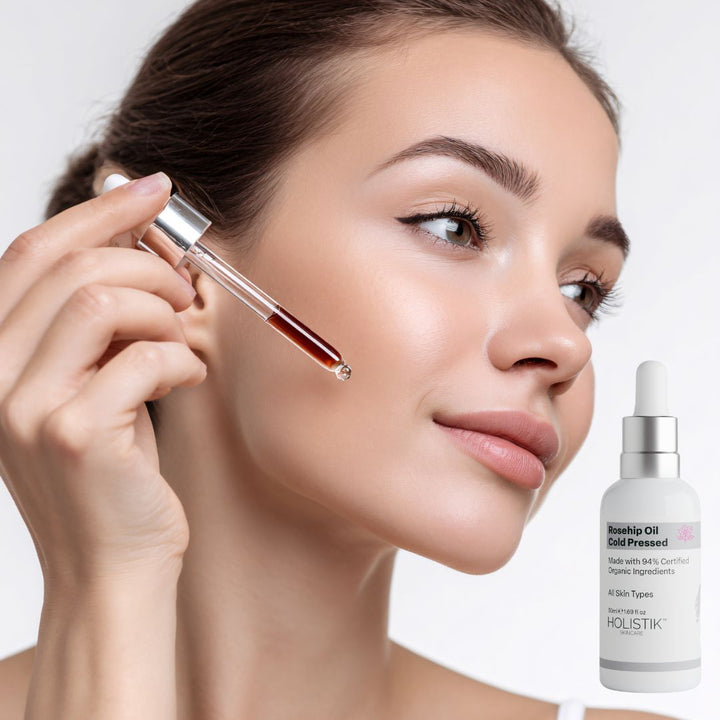 Woman holding a dropper with a skincare product next to a bottle of Holistik Skincare Rosehip Oil